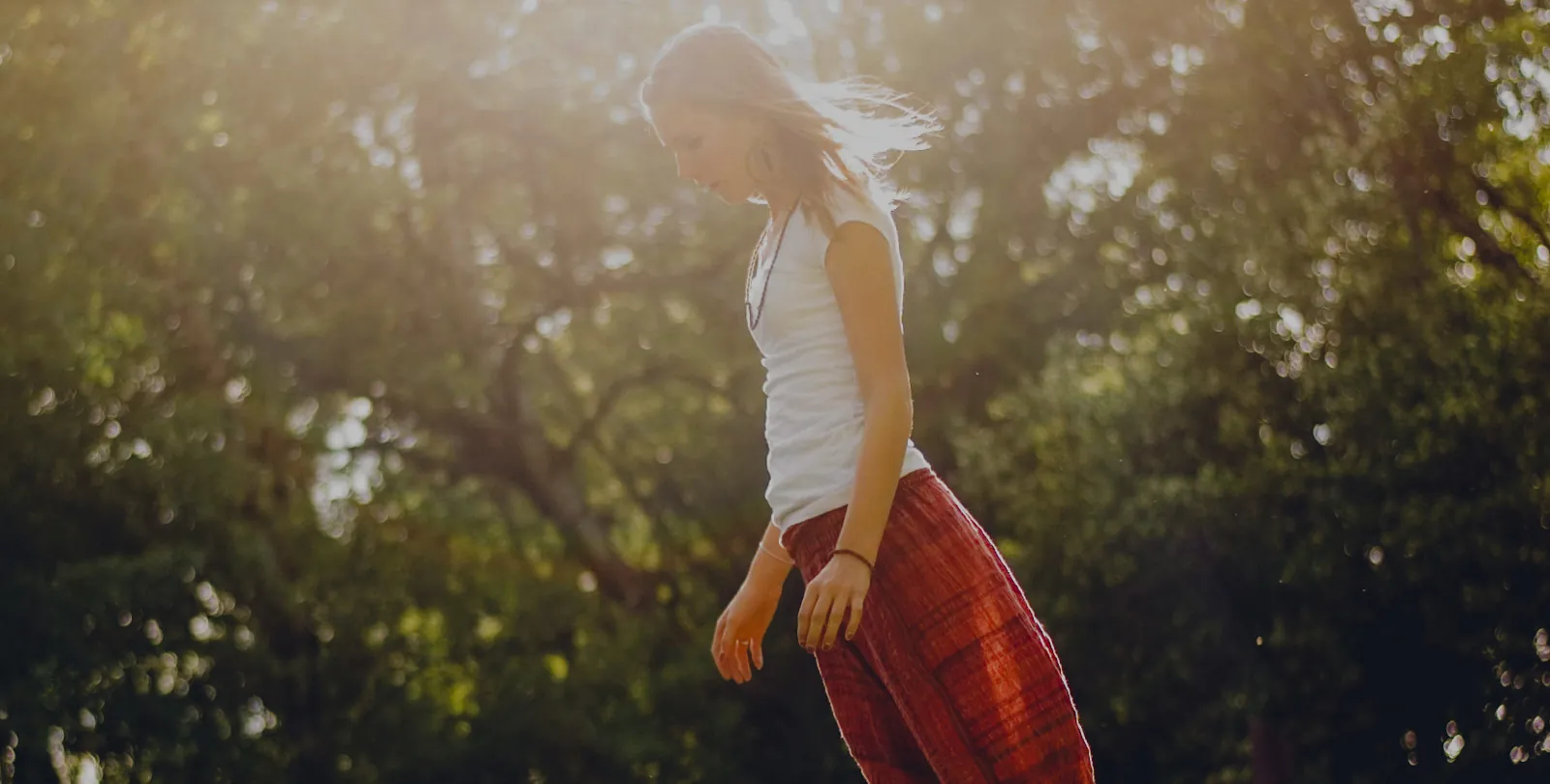 A woman in a long red skirt walking through a sunlit paddock